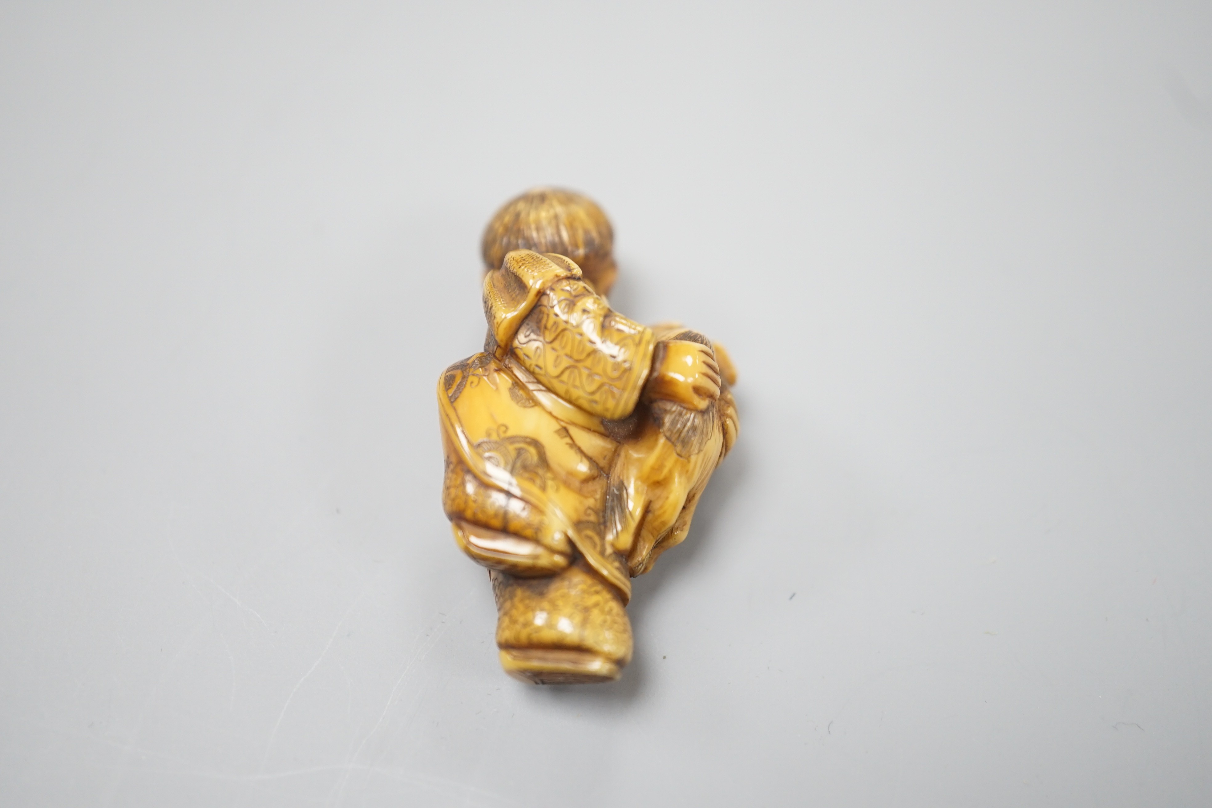 A Japanese ivory netsuke of a dog piggybacking a boy, Meiji period, 3.9cm